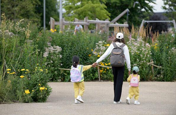 An adult hold the hands of two children as they walk through Queen Elizabeth Olympic Park