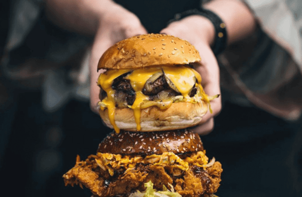 A man holding a meaty burger on top of another burger