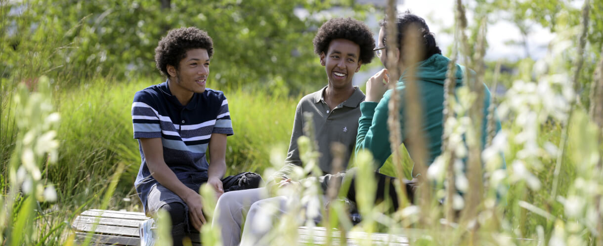 three people sit on a bench in Queen Elizabeth Olympic Park