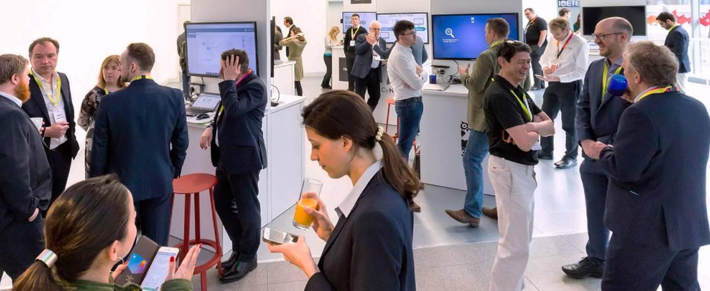 A group of professionals networking in a white room with screens in the background