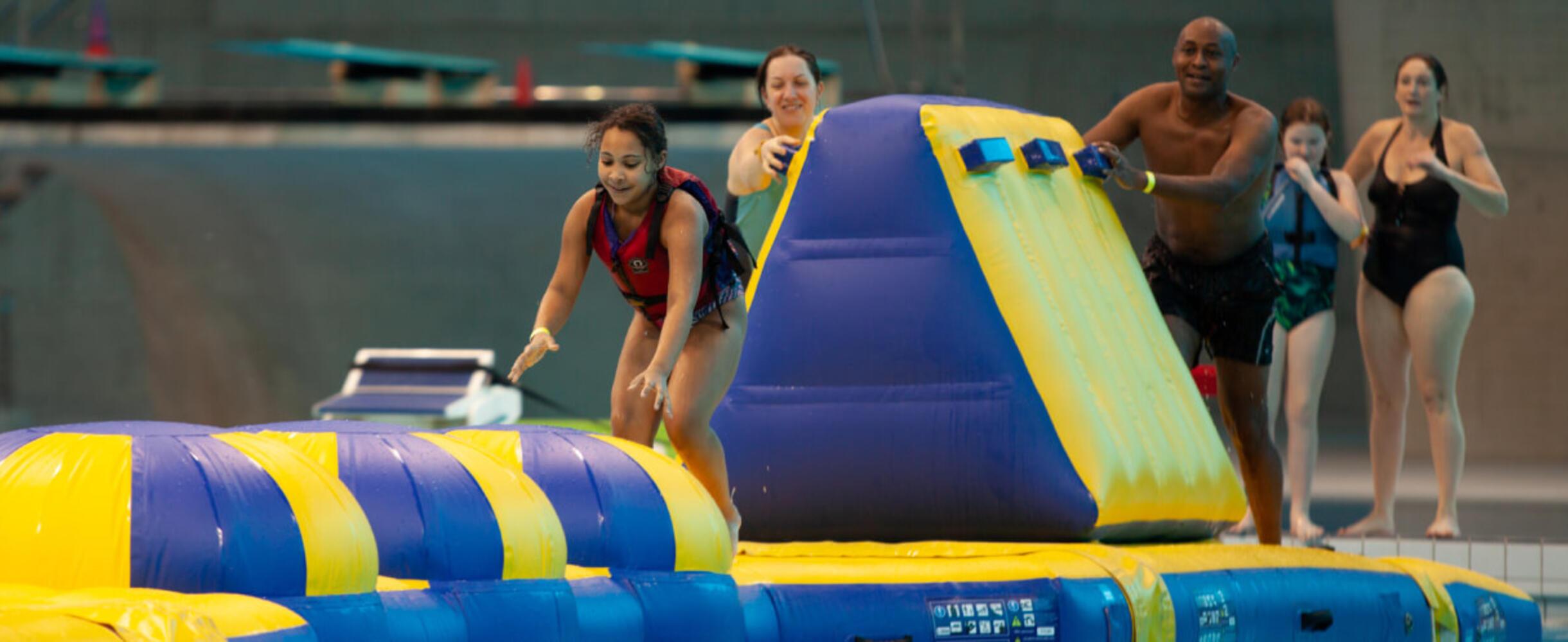 A young girl crawls along the inflatable Aqua Splash with adults looking on