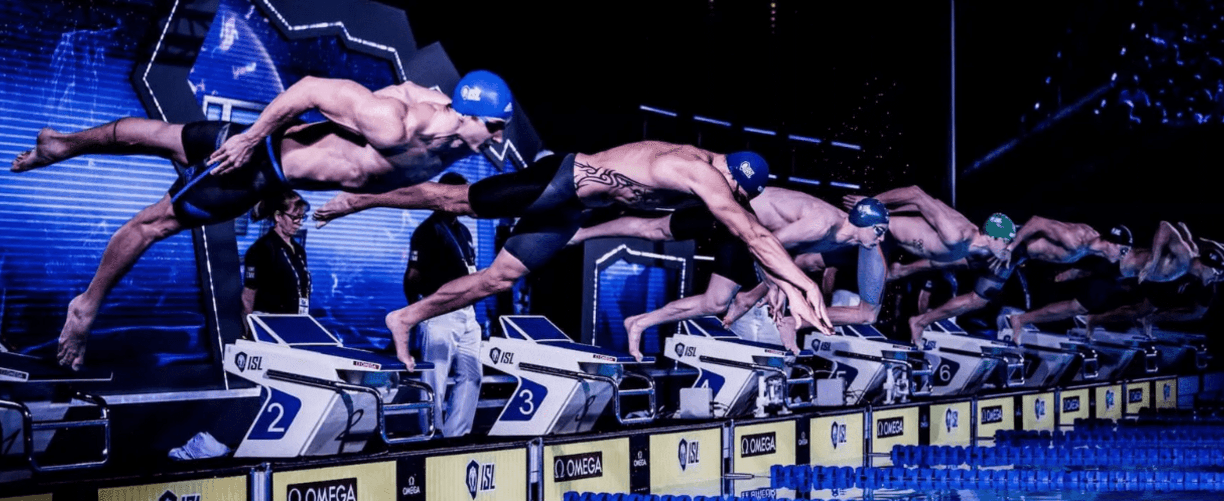 A line of male swimmers diving into the pool at the start of a race