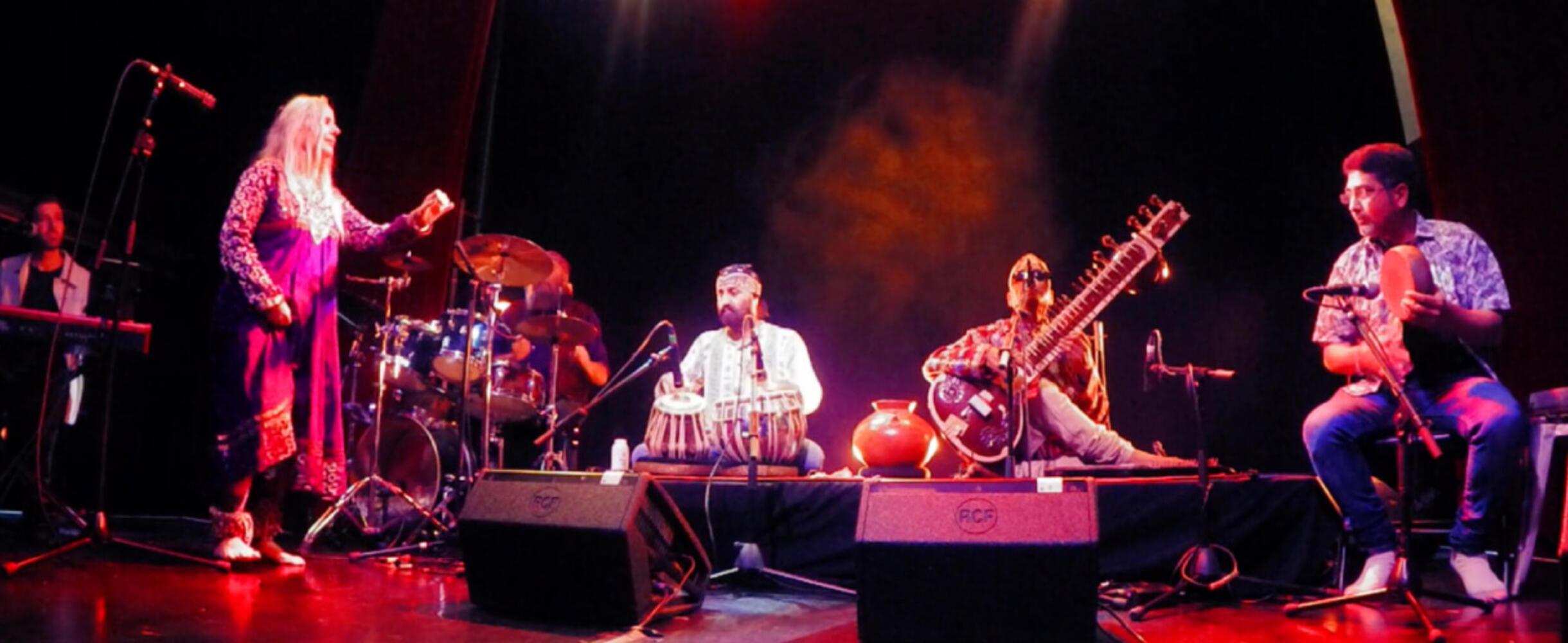 A band with a sitar player in the front play on a stage
