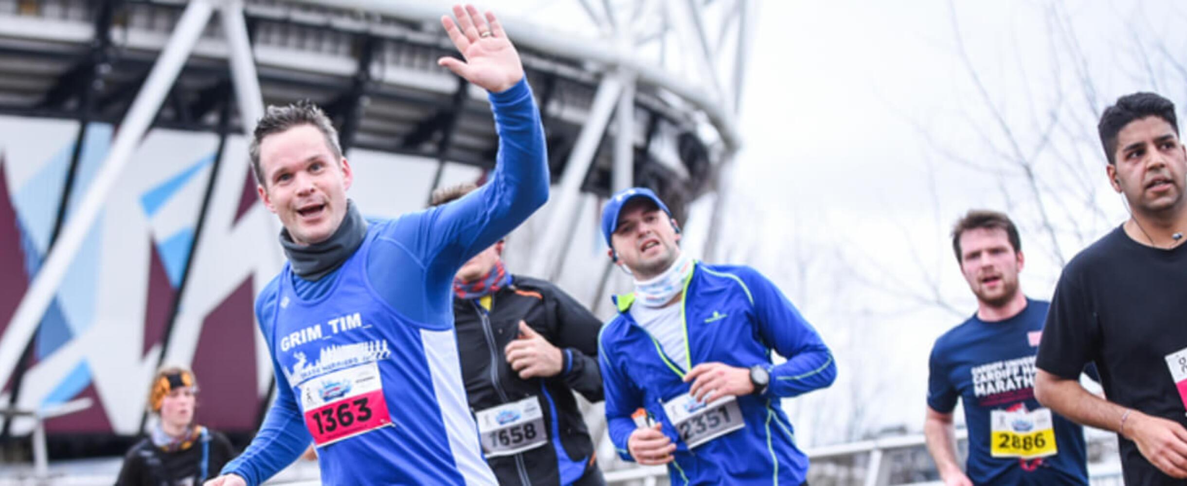 A group of runners smiling to camera with London Stadium in background