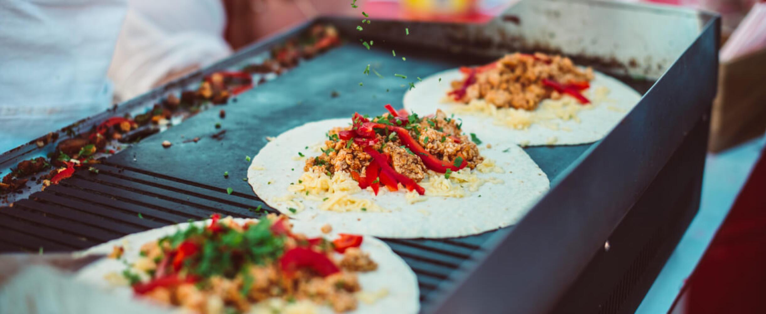 Mexican street food wraps being cooked on a grill outside