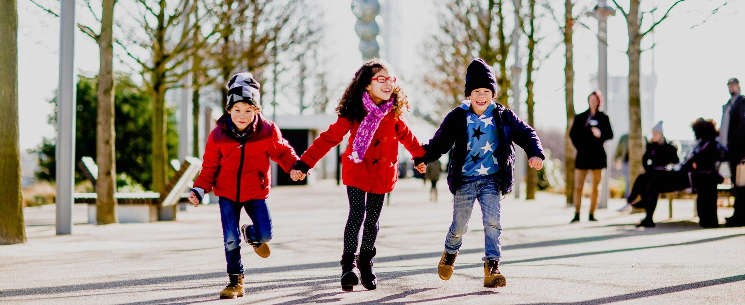 Three children holding hands and smiling on path