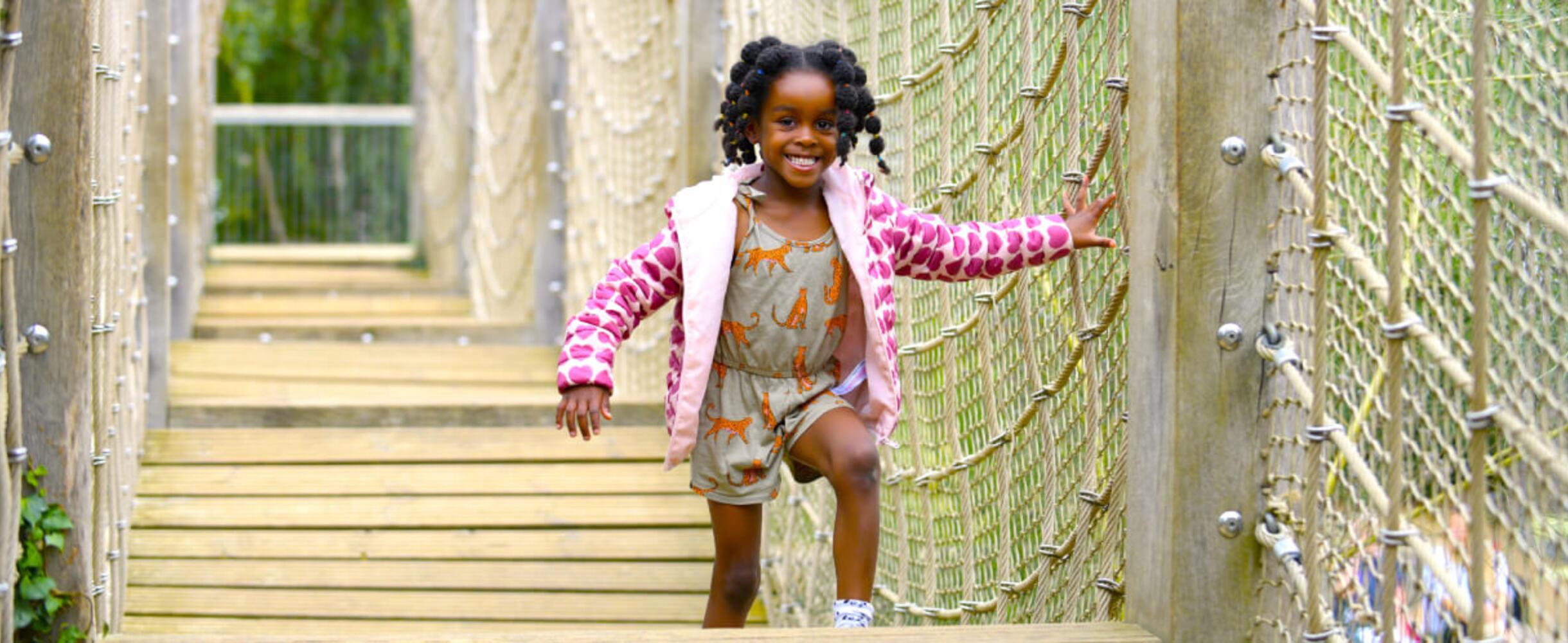 A little girl runs across the rope bridge at Tumbling Bay Playground