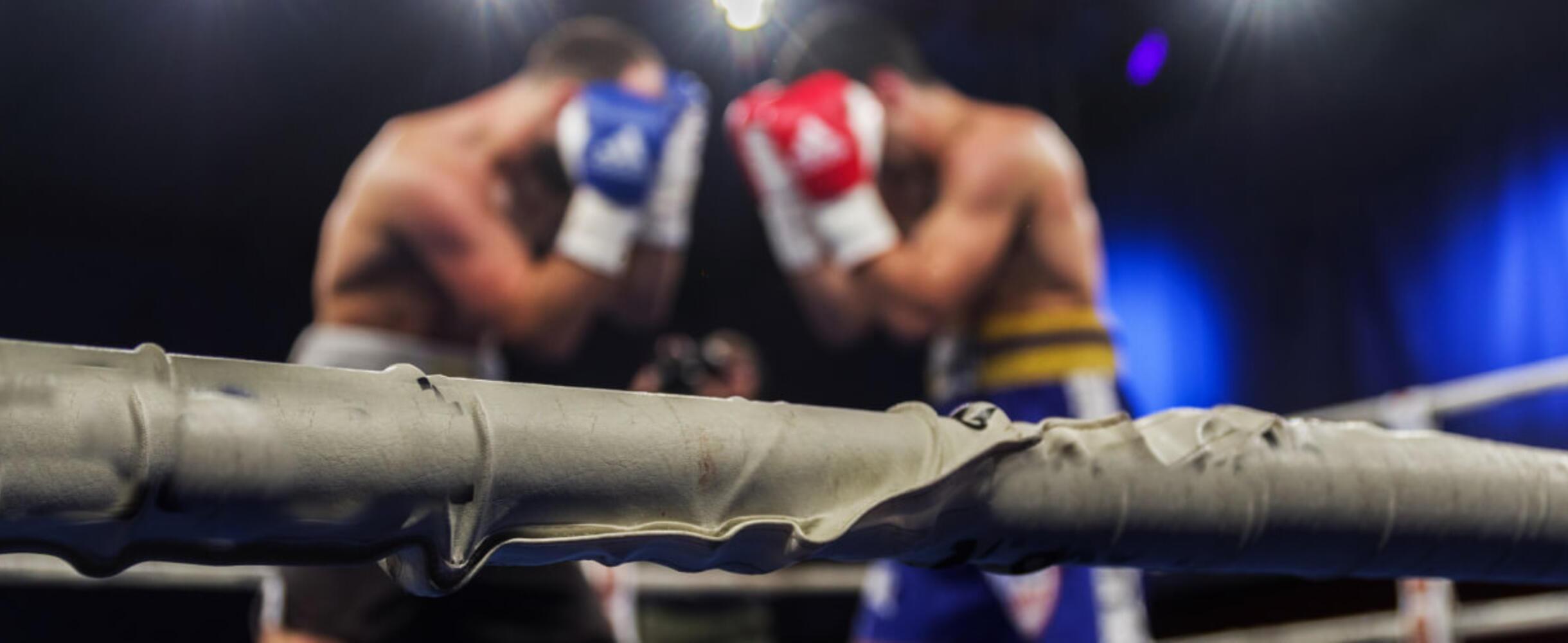 A pair of boxers in a ring stand in defensive stances