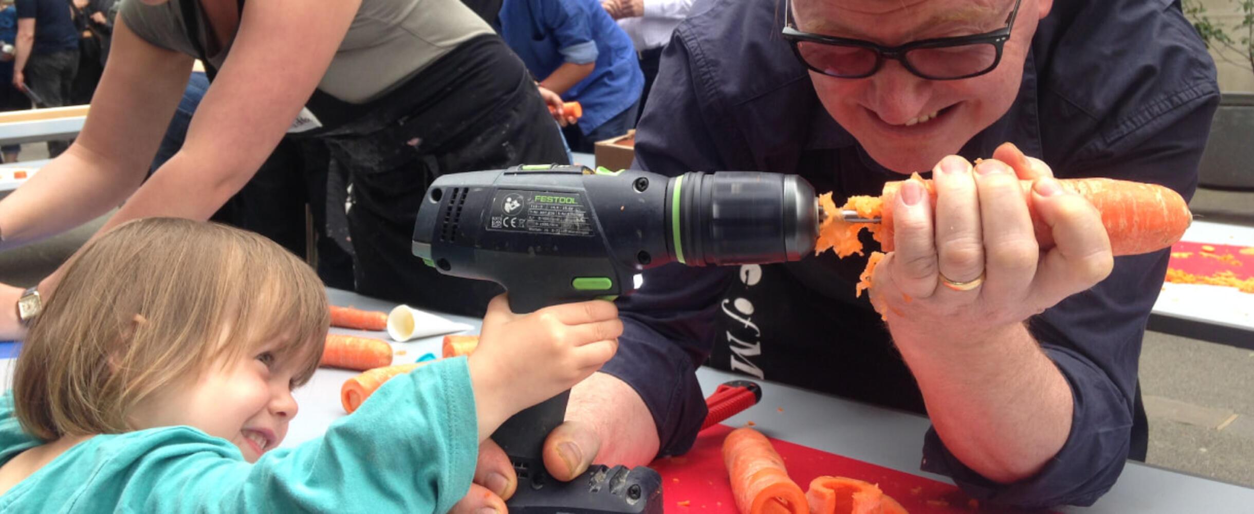 A person holds a carrot on the end of a drill
