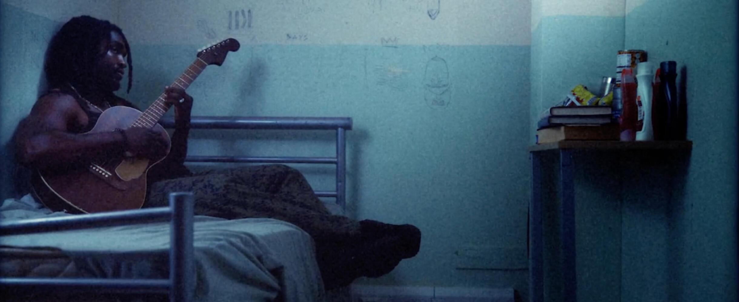 Hak Baker sits on a bed with a guitar