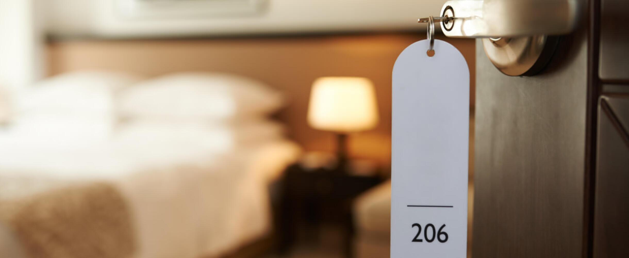 A door opens to a hotel room with key in lock