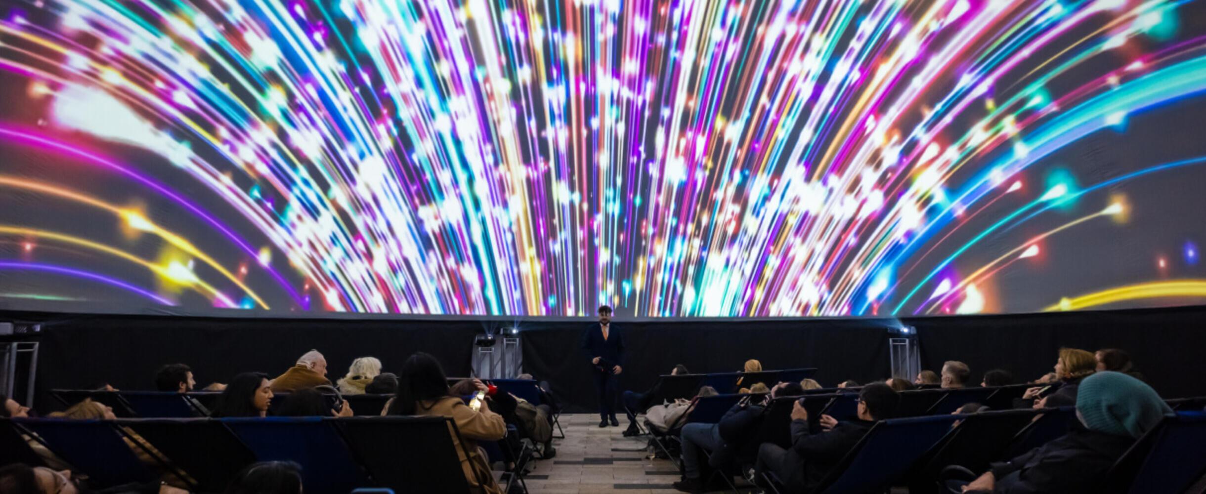 A large planetarium screen lights up with people sat beneath