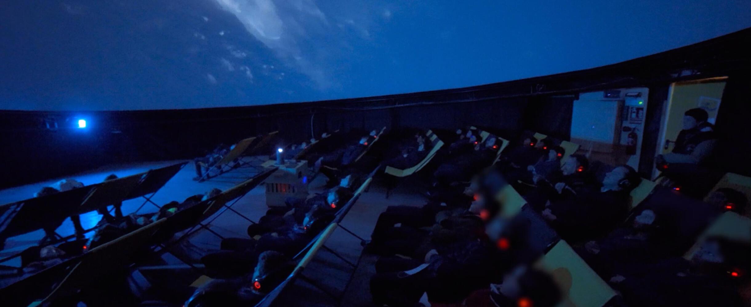 A dark planetarium filled with people looking up at the ceiling.