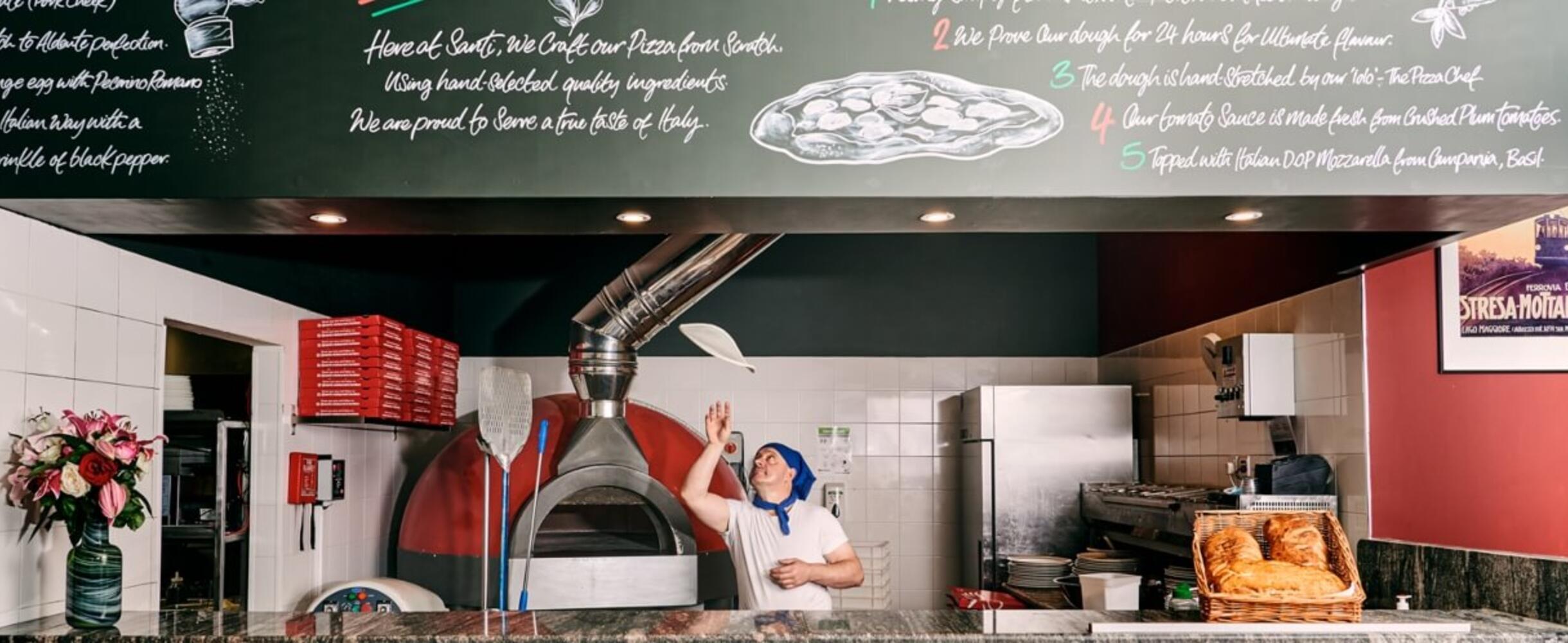 A chef tosses pizza dough in an open kitchen
