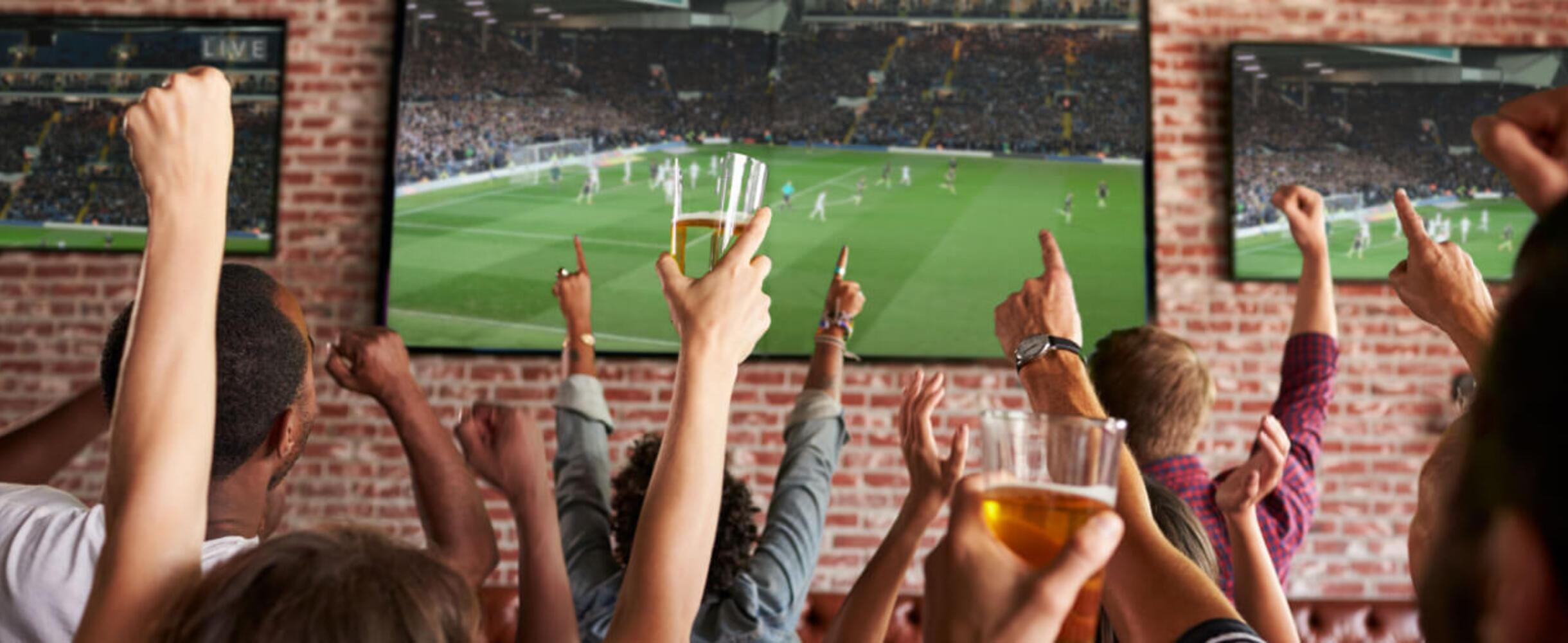 A group of people cheering at a sports screen