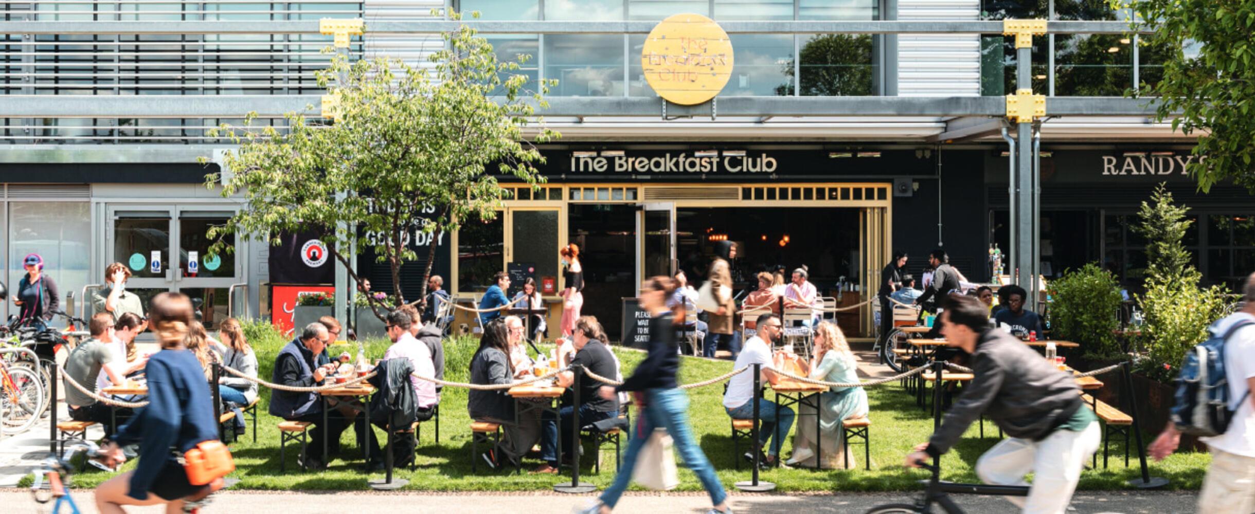 Groups of tables sit outside in the sun out The Breakfast Club Hackney