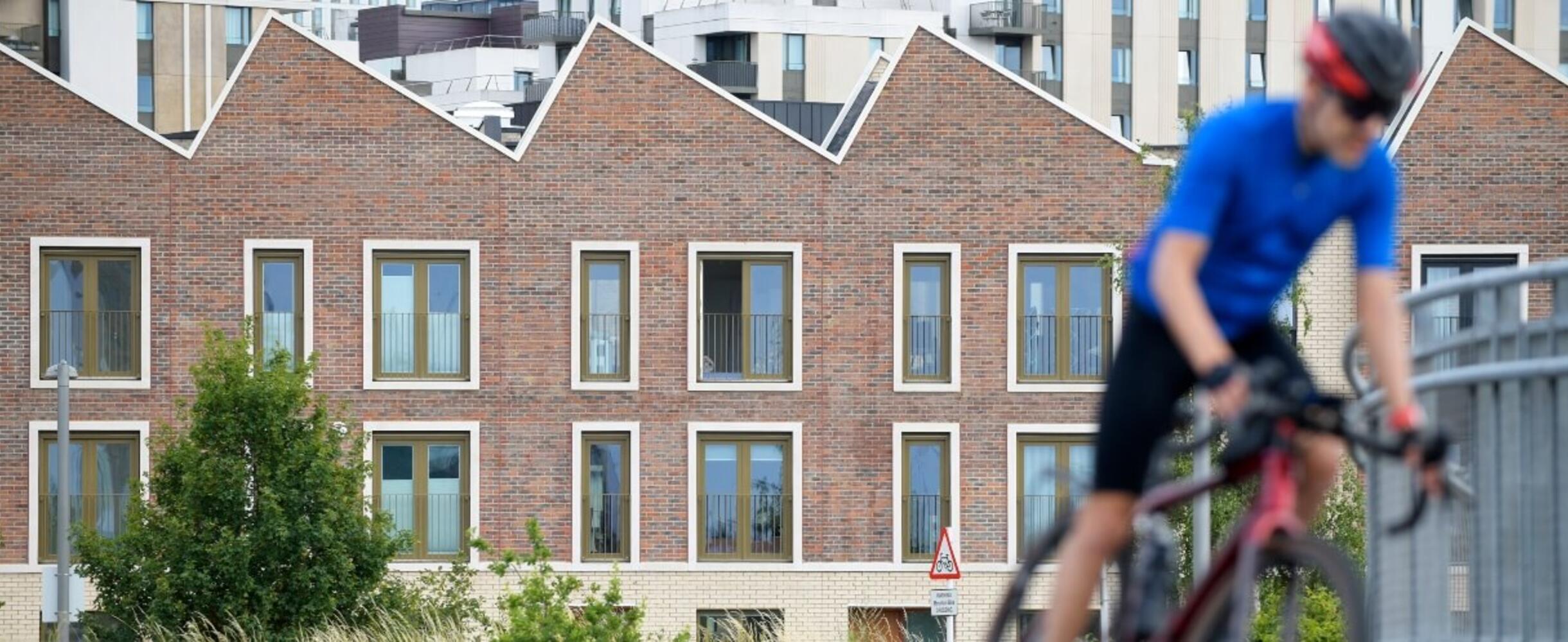 A cyclist goes past housing on Queen Elizabeth Olympic Park