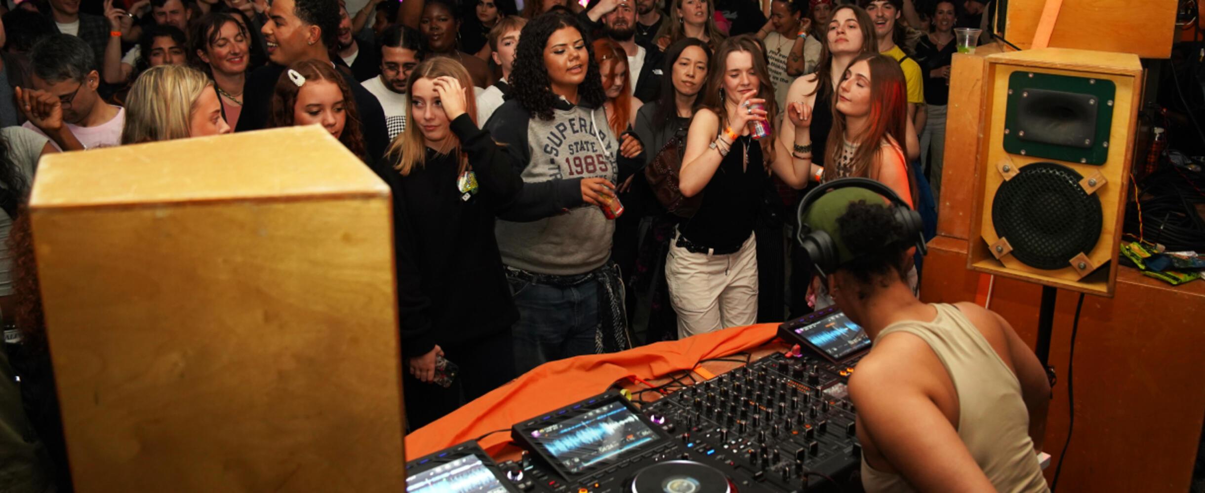 A crowd of people dance in front of a DJ decks