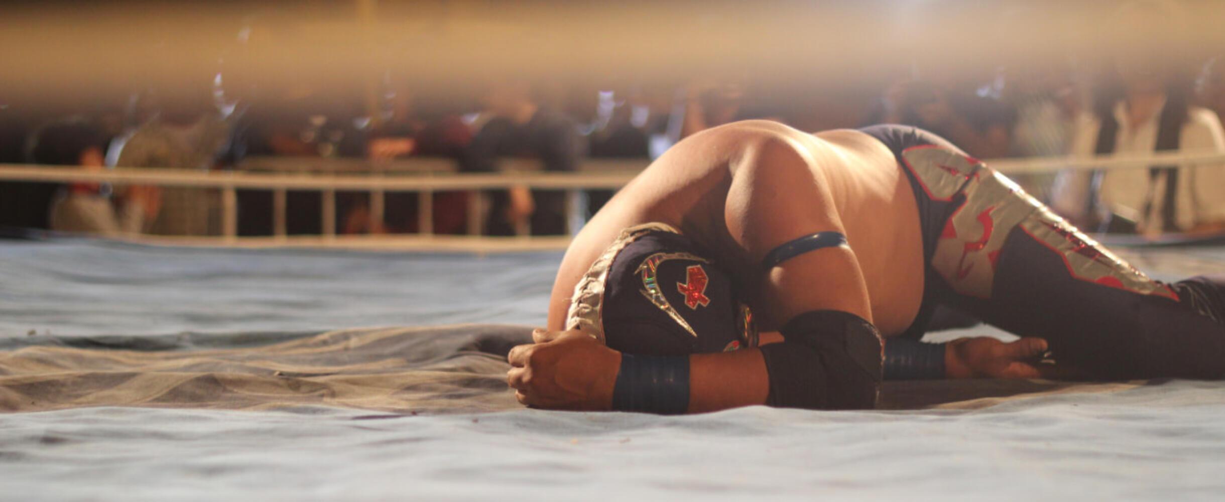 A wrestler lies prone on the canvas of the ring