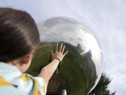 a child reaches towards a mirror ball piece of art