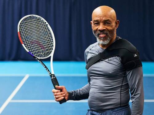 Man posing with Tennis racket with blue tennis court in the background