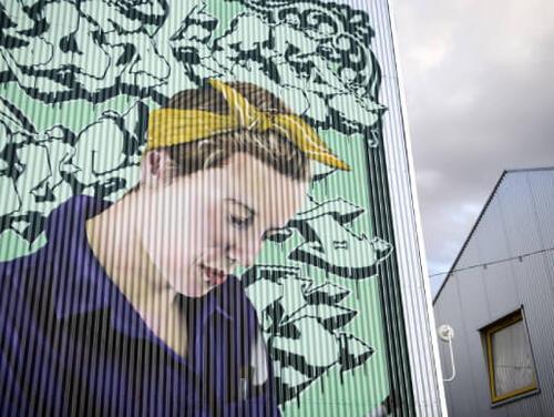 A large drawing on the side of a building of a women with a yellow bow in her hair