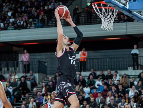 A basketball player reaches up to basket to dunk the ball