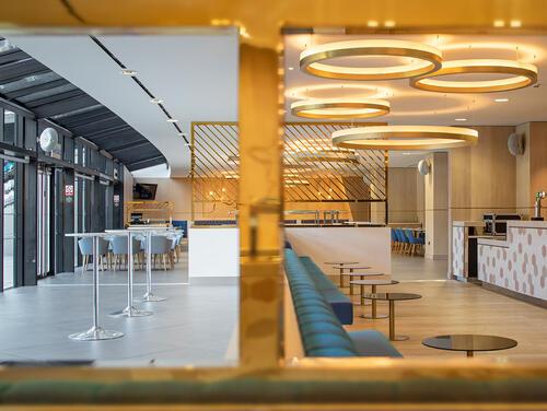 A venue space showing blue couches, gold lighting and features, as well as high tables. 