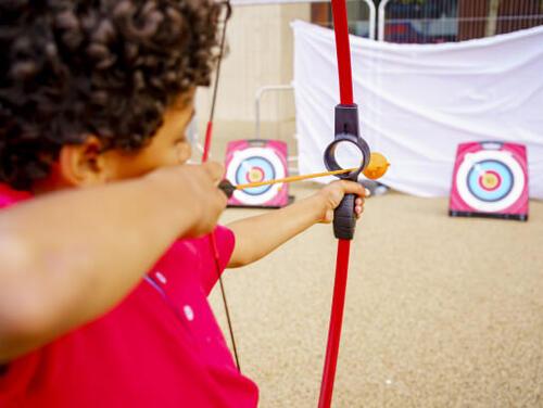 a child aims a plastic bow and arrow at a target Great Get Together