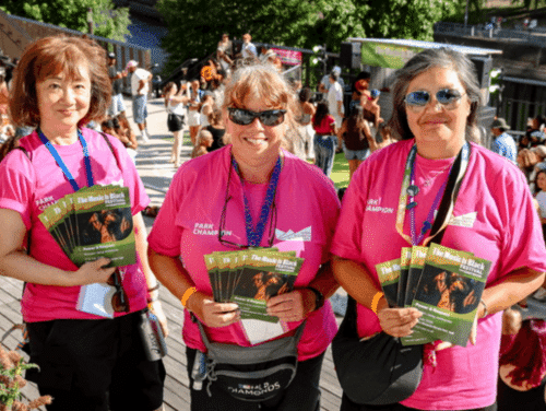 Three women in pink volunteer tshirts holding festival leaflets