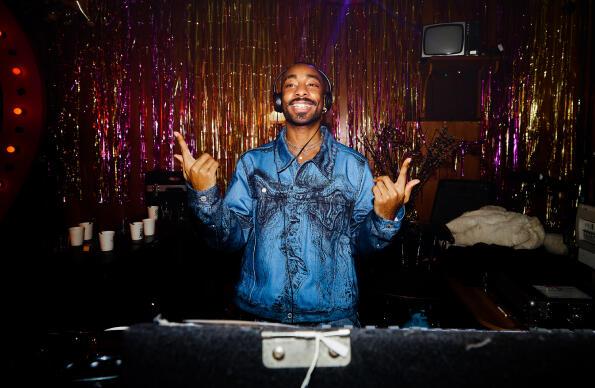 A DJ at a deck with sparkly background behind him