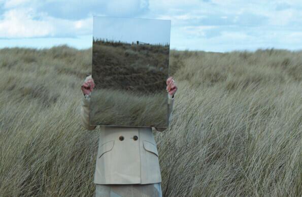 An artist in beige clothing blends into a grassy area with blue sky behind An artist in beige clothing blends into a grassy area with blue sky behind