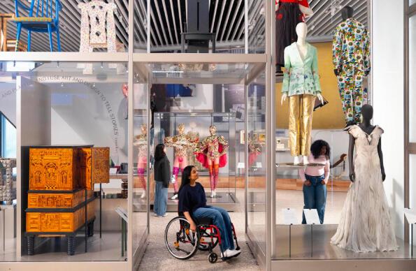 A person using a wheelchair looks at artefacts and fashion items at V&A East Museum