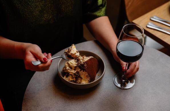 A person eating tiramisu and drinking red wine at Riverside East on Queen Elizabeth Olympic Park A person eating tiramisu and drinking red wine at Riverside East on Queen Elizabeth Olympic Park