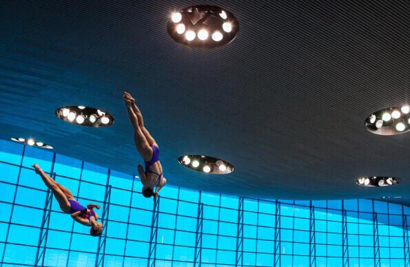 Two divers spin in tandem with ceiling of London Aquatics Centre as a backdrop