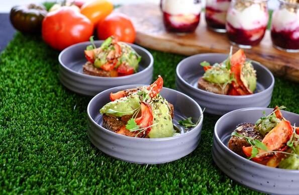 A close up on small bowls of food with vegetables and drinks in the background