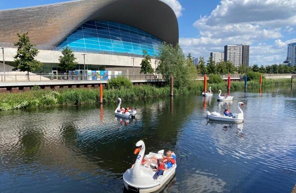 Groups of people ride the swan pedalos on the river outside the London Aquatics Centre
