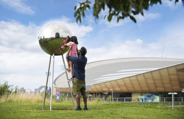 A parent lifts their child up to see a piece of art on the queen elizabeth olympic Park