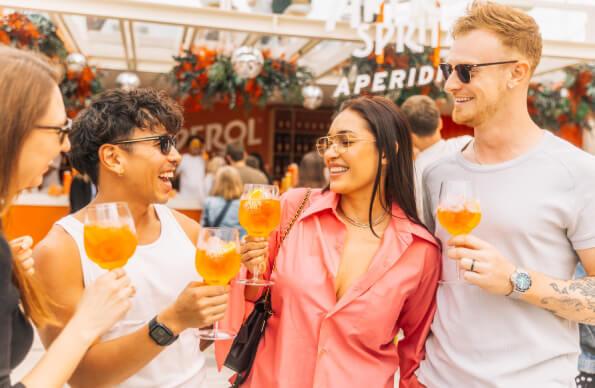4 people stand, holding Aperol Spritz 4 people stand, holding Aperol Spritz