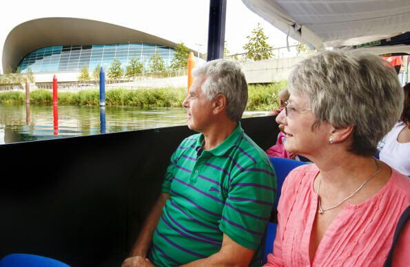An older couple look out the window of the boat whilst on the river next to the London Aquatics Centre