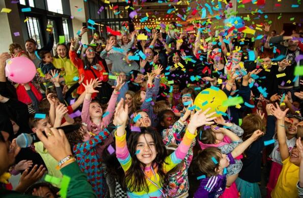 A group of children and parents dance with confetti in the air