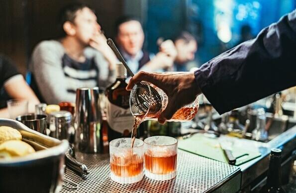 A bartender mixing drinks at a bar as patrons look on