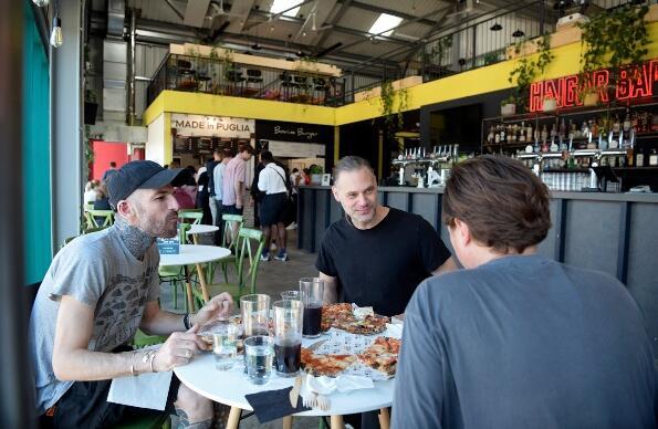Three men chatting and eating inside Hackney Bridge