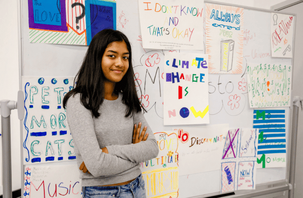 Photo of a girl stood next to a whiteboard full of school drawings
