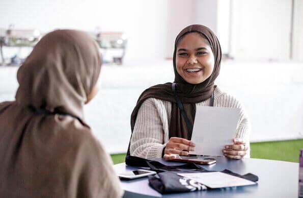 Woman with hijab talks over a table to friend Woman with hijab talks over a table to friend
