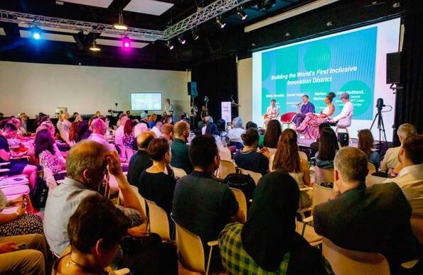 Four people giving a panel discussion in front of a busy and crowded room