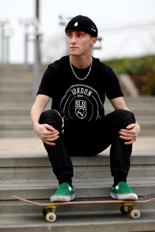 Alex Decunha with skateboard sitting on steps