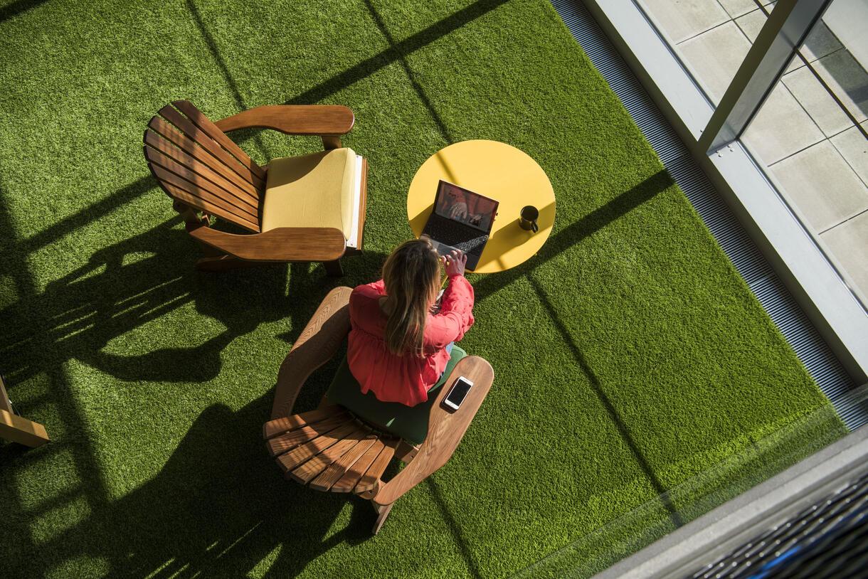An image looking down on a woman working on deck chairs inside a sunny area with fake grass