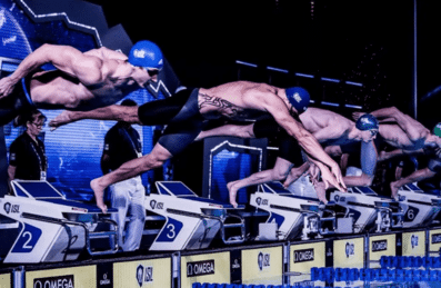 A line of male swimmers diving into the pool at the start of a race