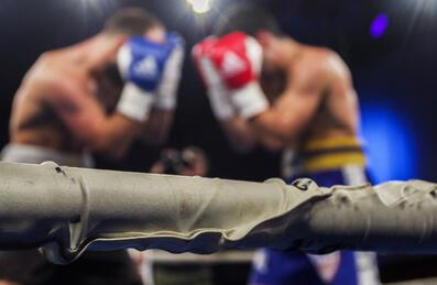 A pair of boxers in a ring stand in defensive stances 